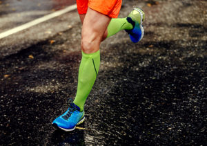 photo of male runner in compression socks running on black asphalt road