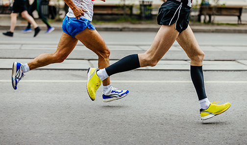 photo of the legs of two male runners, one is wearing black compression stockings